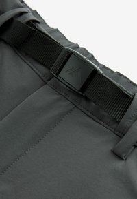 Gros plan d'une ceinture réglable en sangle noire avec boucle en plastique sur la ceinture d'un vêtement en tissu gris foncé.