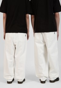 Pantalones anchos blancos con bolsillos traseros, combinados con una camiseta negra. Color sólido, tela suave, corte relajado y longitud hasta el tobillo.