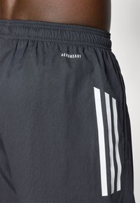 Lettfede sorte atletiske shorts med elastisk talje, der har hvide striber ned ad siden og et "AEROREADY" logo nær taljen.