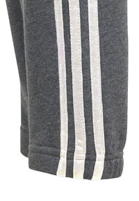 Grå sweatpants med en mjuk textur har tre vertikala vita ränder längs sidan. Benkanten är sydd, vilket säkerställer hållbarhet.