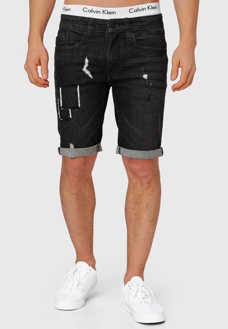 Shorts en denim noir avec déchirures, ourlets roulés et ceinture blanche Calvin Klein. Design épuré avec plusieurs détails de patch.