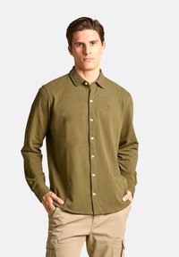 Camicia a maniche lunghe color verde oliva in cotone, con colletto a camicia e logo ricamato sul petto. Bottoni bianchi e orlo dritto.