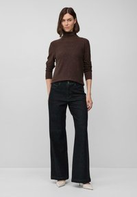 Maglione a collo alto marrone maculato abbinato a jeans scuri a vita alta; modella che indossa décolleté beige a punta, sfondo neutro.
