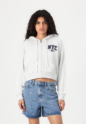 Gray zip-up cropped hoodie with white drawstrings and 'NYC 22' graphic. Paired with blue denim shorts featuring floral embroidery.