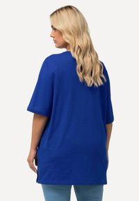 Blue oversized t-shirt, short sleeves, smooth fabric, rounded neckline, side slits at the hem, designed for a relaxed fit.