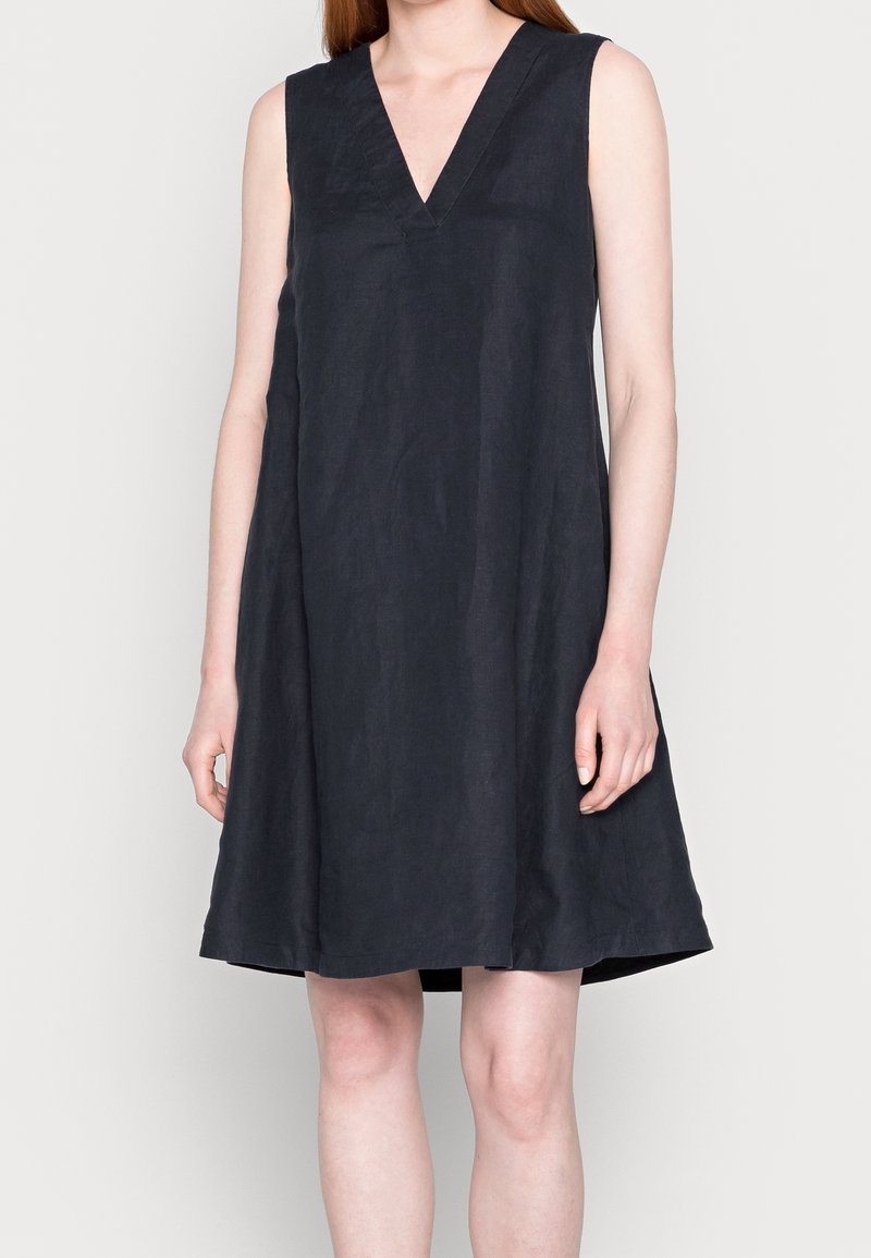 Robe noire sans manches avec un décolleté en V, fabriquée dans un tissu texturé. Silhouette évasée atteignant le mi-cuisse, sans accents supplémentaires.