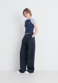 Haut bleu marine à manches courtes avec un col bleu clair, associé à un pantalon large noir. Le mannequin porte des baskets blanches ; design minimaliste.