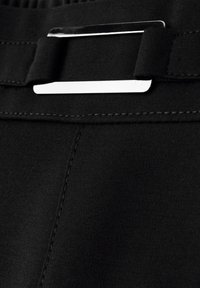 Gros plan sur un tissu noir avec une boucle de ceinture rectangulaire argentée et des détails de couture sur la ceinture d'un vêtement.