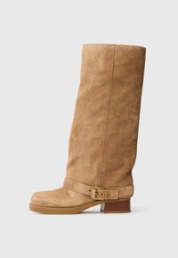 Stivale medio in suede color tan con tacco basso e impilato, punta arrotondata e una cinghia regolabile con una fibbia dorata intorno alla caviglia.