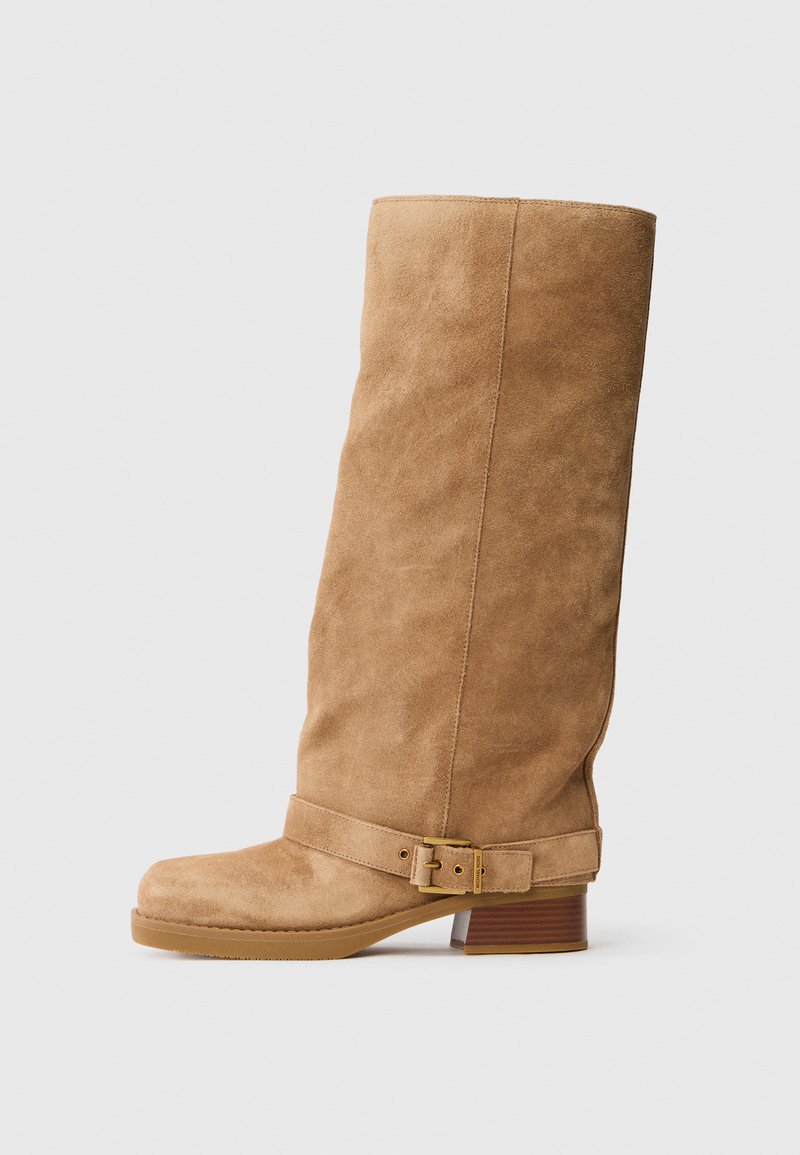 Stivale medio in suede color tan con tacco basso e impilato, punta arrotondata e una cinghia regolabile con una fibbia dorata intorno alla caviglia.