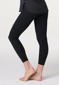 Leggings neri realizzati in tessuto elastico e morbido, caratterizzati da un design aderente e cuciture piatte per il massimo comfort. Lunghezza fino al polpaccio senza motivi o decorazioni.