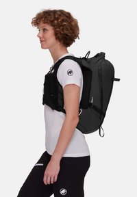 Czarny i szary plecak z geometrycznym wzorem, siateczkowymi akcentami, regulowanymi paskami i smukłym kształtem, noszony na białej koszuli.