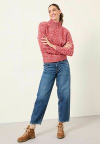 Rot-weißer, gepunkteter Rollkragenpullover, kombiniert mit hochtaillierten blauen Jeans und braunen, mit Fell gefütterten Knöchelstiefeln. Strukturierter, gemütlicher Stoff.