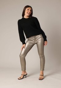 Zwarte gebreide trui met ribbeltextuur en scalloped halslijn, gecombineerd met glanzende metallic gouden fitted broek en zwarte strappy hakken.