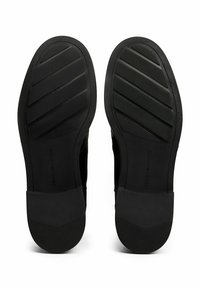 Semelles de chaussures en caoutchouc noir avec des rainures horizontales et une texture lisse. Présente une section de talon angulaire et audacieuse. Marque claire sur le côté.