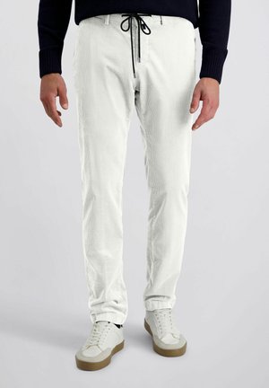 Witte corduroy broek met een gestructureerde afwerking, slim fit, en zwarte trekkoord in de taille. Gecombineerd met lichte sneakers met beige accenten.