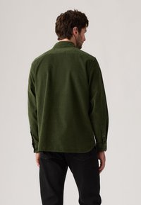 Green corduroy shirt with a classic collar, long sleeves, and button cuffs. Tailored fit with a slightly curved hem and textured fabric.
