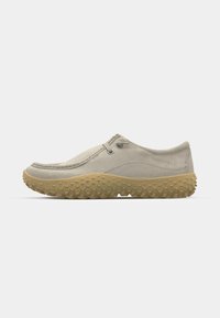Beige slip-on sko med avrundet tå, teksturert gummisåle og to aksentgjennomføringer. Myk tekstiloverdel med subtile sømdetaljer.