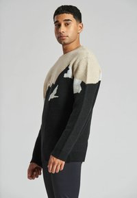 Strickpullover mit schwarzem Körper und einem creme- und grau-farbenen Bergmuster im oberen Bereich, rundem Ausschnitt und gerippten Bündchen.