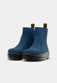 Blue ankle boots made of textured material, featuring a thick black sole with yellow stitching and pull tabs for easy wearing.