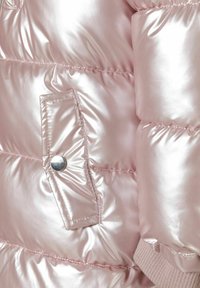 Reflekterande rosa puffer-jacka i närbild med quiltad textur, sidoficka med knapp för att stänga samt ribbad stickad manschettdetalj.
