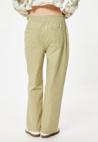 Helle olivgrüne Hose mit elastischem Bund, zwei Gesäßtaschen und geradem Bein. Glattes Material mit einem leicht matten Finish.