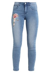 Jeans skinny de mezclilla azul claro con un diseño ajustado, que presentan patrones florales bordados multicolores en el muslo izquierdo.