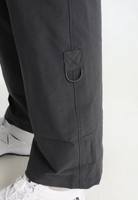 Svarta, lätta, vattenavvisande byxor med en slät textur, som har en sidögladetalj och stickade accenter. Bärs med vita sportskor.