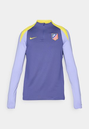Paarse sportieve lange mouwen shirt met gele accenten, half-rits kraag en een teamlogo op de linkerkant van de borst. Gemaakt van gladde stof.