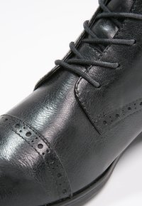 Černé kožené šněrovací boty s lehce lesklým povrchem. Obsahují brogue detaily na špičce a po straně. Hladká textura a klasický design.