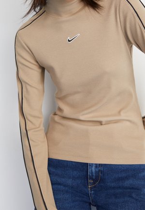 Beżowy prążkowany golf z czarnymi paskami na rękawach i białym logo Nike, noszony z niebieskimi dżinsami, widoczna środkowa część.