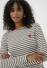 Gestreiftes Langarmoberteil in Creme mit braunen Streifen, mit einer kleinen roten Herzstickerei auf der Brust. Weiches Baumwollmaterial, lässige Passform.