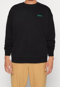 Černá mikina s dlouhými rukávy, žebrovanými manžetami a spodním lemem, s zeleným vyšívaným textem na hrudi. Měkká, hladká textilie.