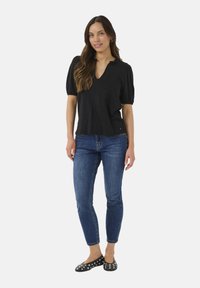 Black linen top with a V-neck and short puffed sleeves, paired with blue skinny jeans and black flats featuring silver studs.
