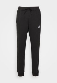 Svarta Adidas joggingsbyxor med elastisk midja, dragsnöre, ribbade muddar, vitt logo på låret och två vita ränder längs yttre sidan av benen.