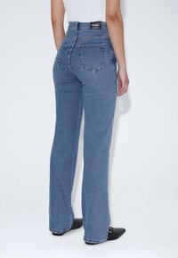 Jeans de denim azul de tiro alto con pierna recta, que cuentan con dos bolsillos traseros y una etiqueta de marca negra en la cinturilla.