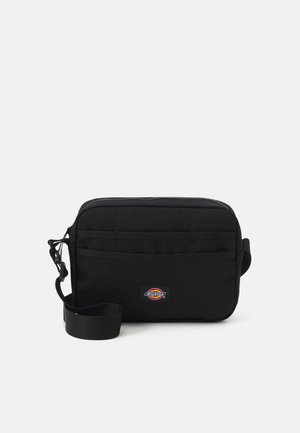 Borsa a tracolla nera in tessuto con chiusura a zip, tracolla regolabile e tasca frontale. Presenta una patch con logo sulla parte anteriore.