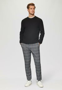 Schwarzer strukturierten Pullover und graue karierten Hose mit weißen Sneakern. Das Outfit kombiniert glatte und gemusterte Stoffe mit einer taillierten Passform.
