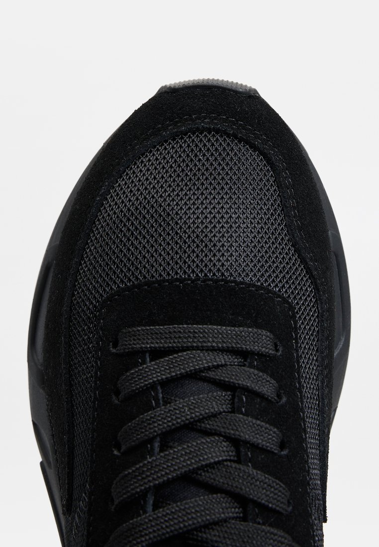 Baskets noires avec un dessus en mesh et en daim, bout rond, six oeillets avec des lacets plats, et une semelle en caoutchouc texturé.