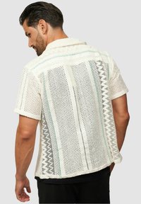 Weißes kurzärmeliges Hemd mit offenem Gewebedesign, welches Streifen in Blau- und Grautönen zeigt, kontrastierender Textur und einem Kragen.