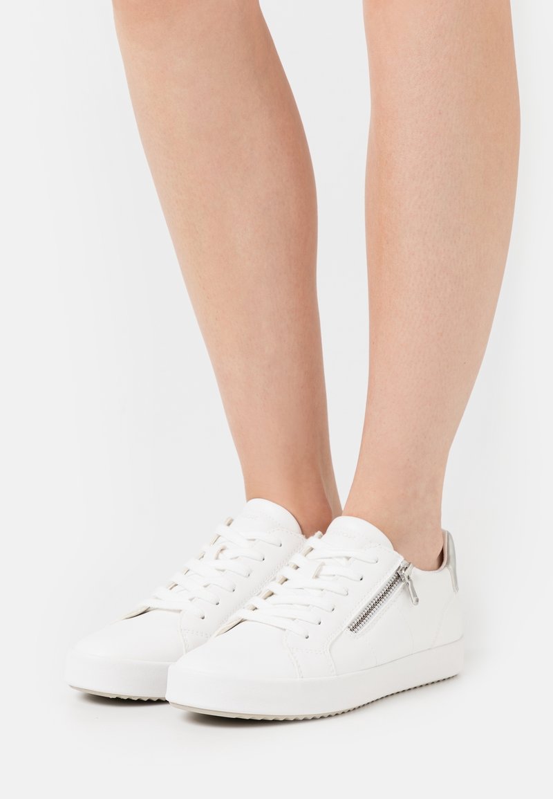 Baskets blanches en cuir lisse, dotées d'une fermeture éclair latérale et de lacets plats. Bout arrondi et semelle en caoutchouc texturée. Design minimaliste.
