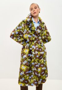 Palton din blană artificială cu un model floral vibrant în nuanțe de verde, maro și albastru, având un rever larg și o curea asortată, cu un design de lungime medie.