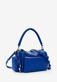 Blaue Lederhandtasche mit strukturierter Oberfläche, ausgestattet mit geflochtenem Griff, Reißverschlussfächern und dem prägenden "Desigual"-Logo an der Seite.