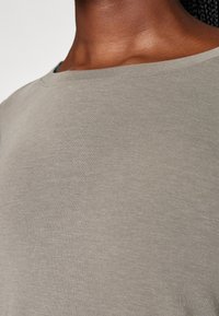 Světle šedé, měkké bavlněné tričko s kulatým výstřihem a krátkými rukávy, které má hladkou strukturu a minimální pružnost.