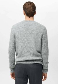 Maglione grigio con motivo a spina di pesce testurizzato, polsini e orlo a costine e scollatura classica a girocollo. Indossato con pantaloni scuri su misura.