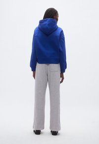 Modrá mikina s kapucňou orezaná po páse, s predným vreckom a sivé široké tepláky. Hladká tkanina, nastaviteľná kapucňa, minimalistický dizajn, voľný strih.