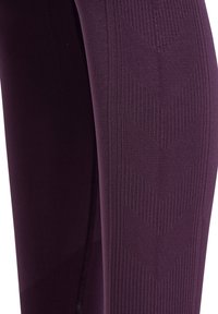 Dunkelviolette Leggings mit einer glatten Textur, die vertikale Rippdetails und Zickzackmuster an den Seiten aufweisen.