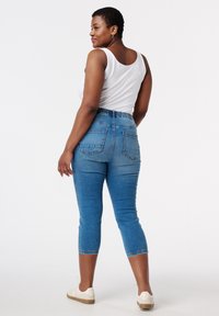 Pantalon capri en denim bleu avec une taille haute élastique, deux poches arrière et un design de jambe effilée. Assorti à un débardeur blanc et des chaussures légères.