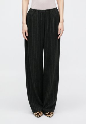 Pantalons noirs à rayures larges avec une taille élastique, texture douce, associés à des talons en léopard.