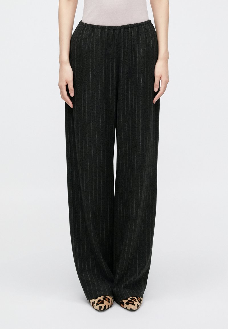 Zwarte pantalon met brede pijpen en streepjes, uitgerust met een elastische tailleband en een zachte textuur, gecombineerd met leopardenprint hakken.